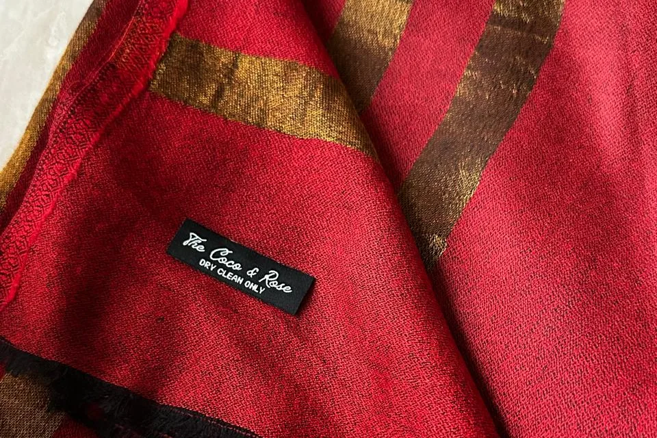 A folded red-and-gold stole with its woven label showing: The Coco & Rose, dry clean only